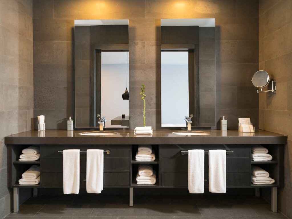 Stylish modern bathroom interior with twin mirrors and towels arranged over sleek dark countertops.